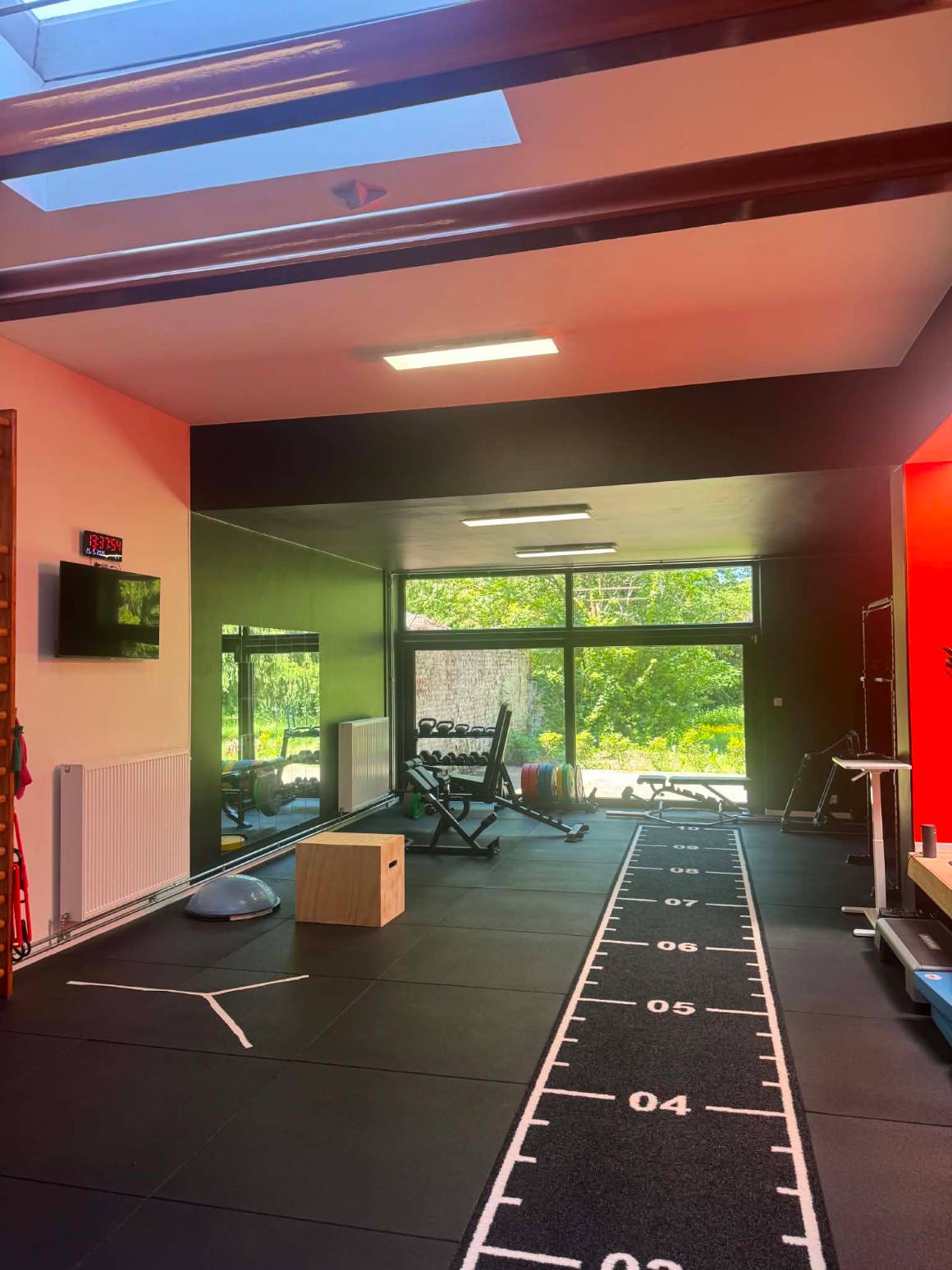 Le fond du plateau technique de KINE+ : miroir mural, box de saut, bosu et baie vitrée ouverte sur le jardin